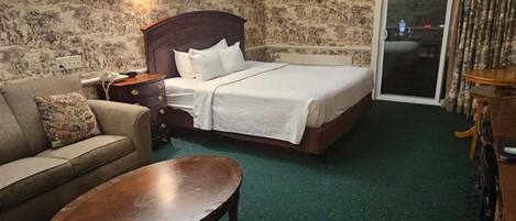 A hotel room with a bed, a sofa, a small table, and a carpeted floor.