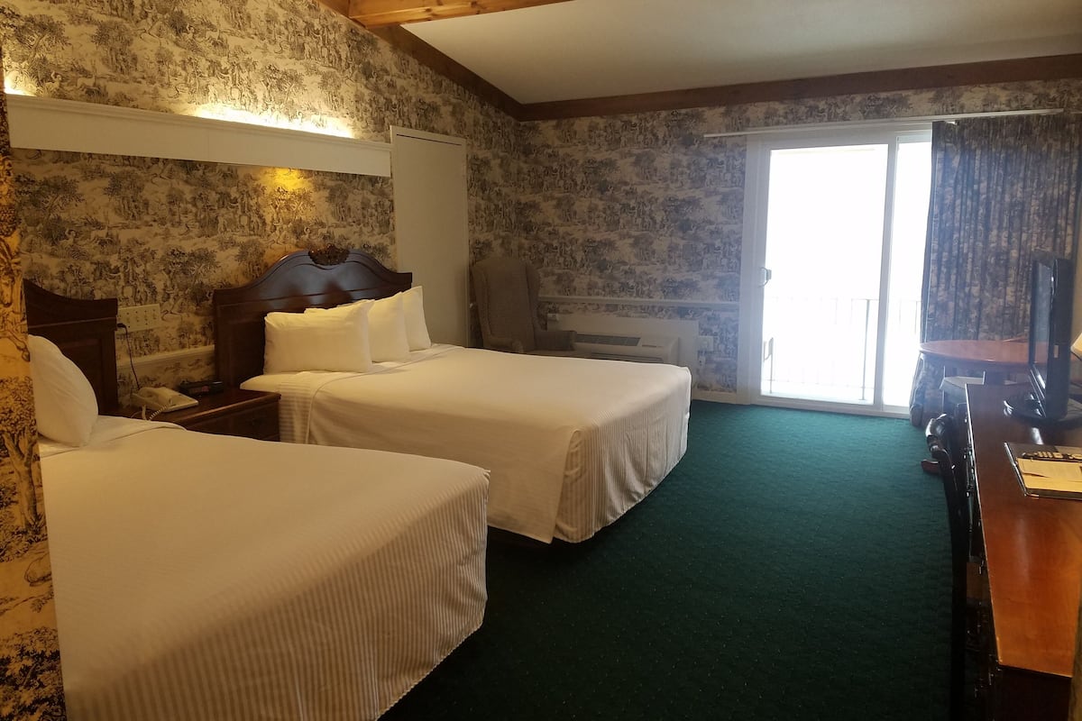 A hotel room with two beds, a desk, a chair, a TV, and a large window.