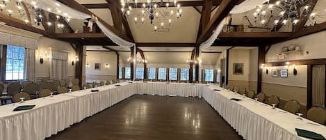 A large conference room with a long table, chandeliers, and wooden beams.
