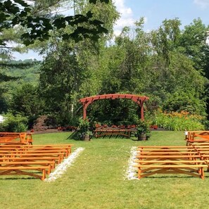 Une cérémonie de mariage est mise en place avec une arche rouge et des bancs en bois disposés en rangées.