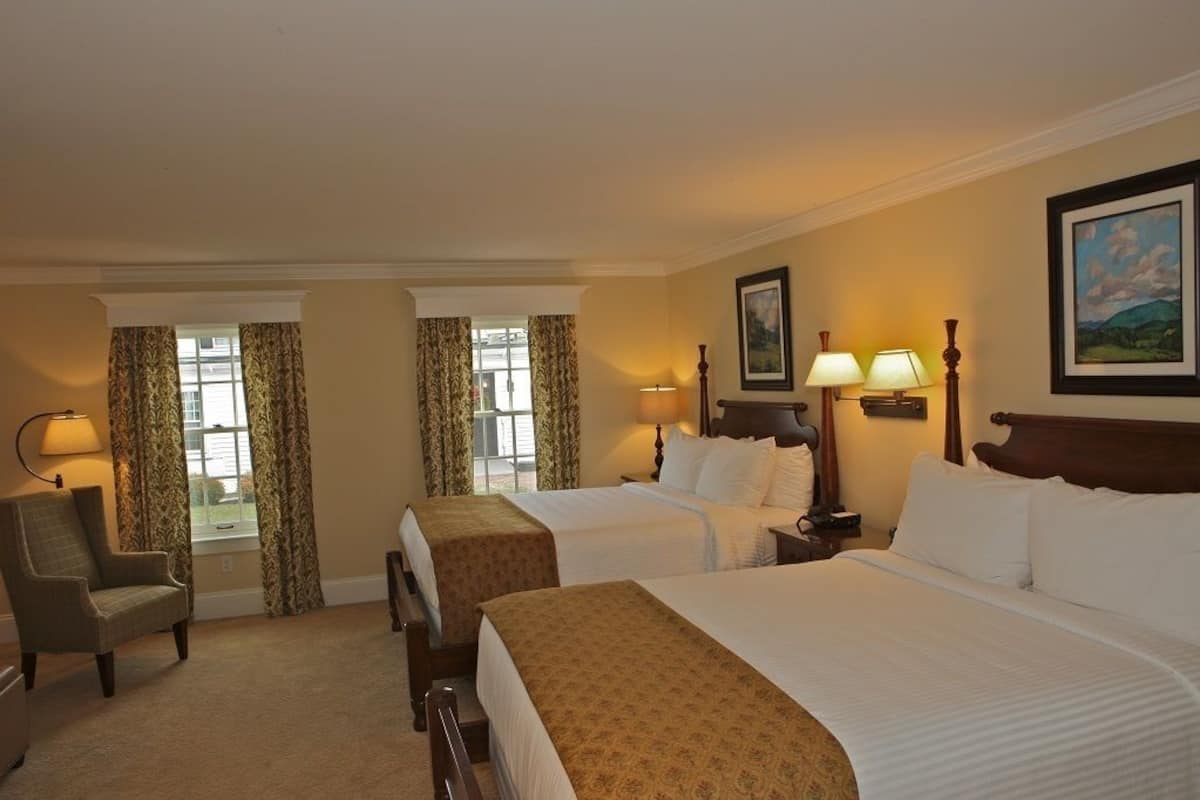 A hotel room with two beds, a chair, a lamp, and a painting on the wall.