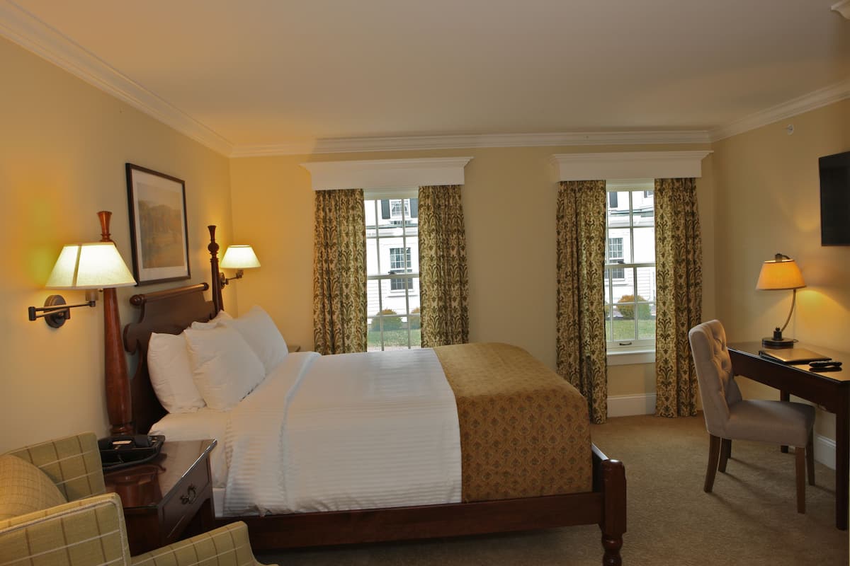 A hotel room with a large bed, two bedside lamps, a desk with a chair, and a window with curtains.