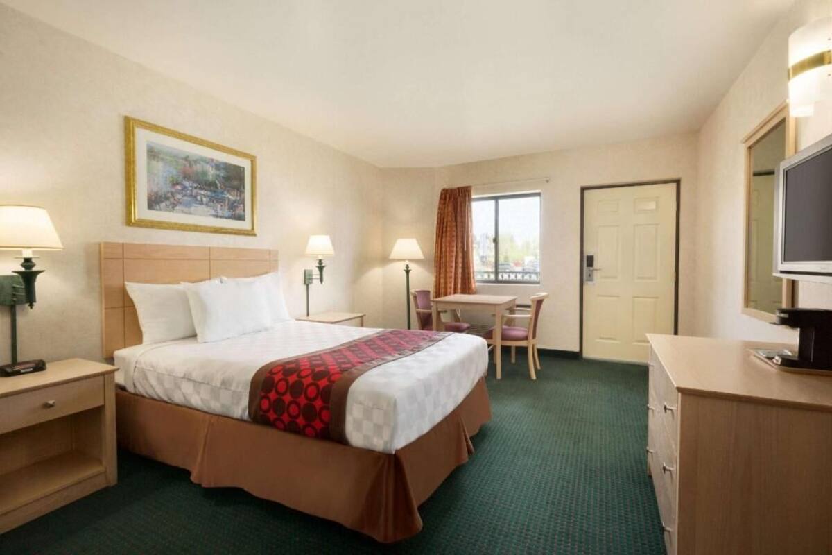 A hotel room with a bed, desk, chair, TV, and a painting on the wall.