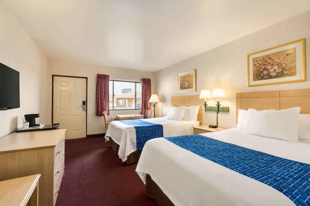 A hotel room with two beds, a desk, a TV, and a window with curtains.