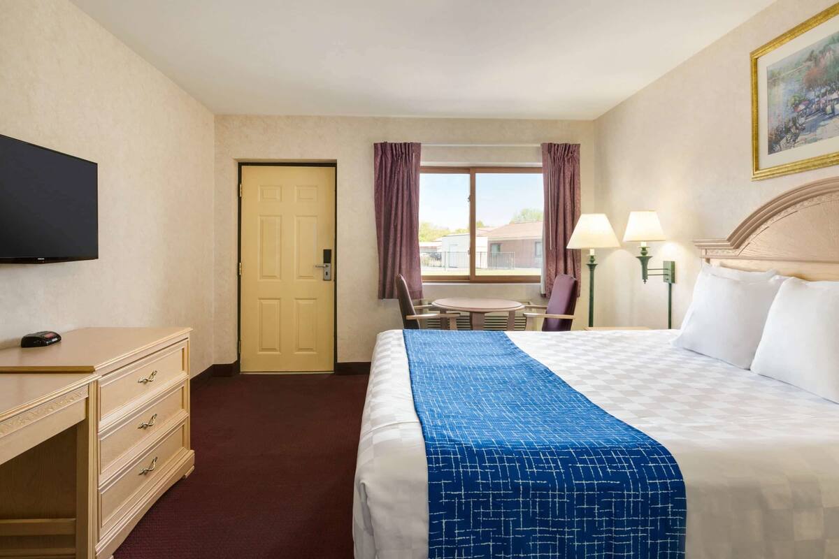 A hotel room with a bed, a desk, a chair, a TV, and a window with curtains.