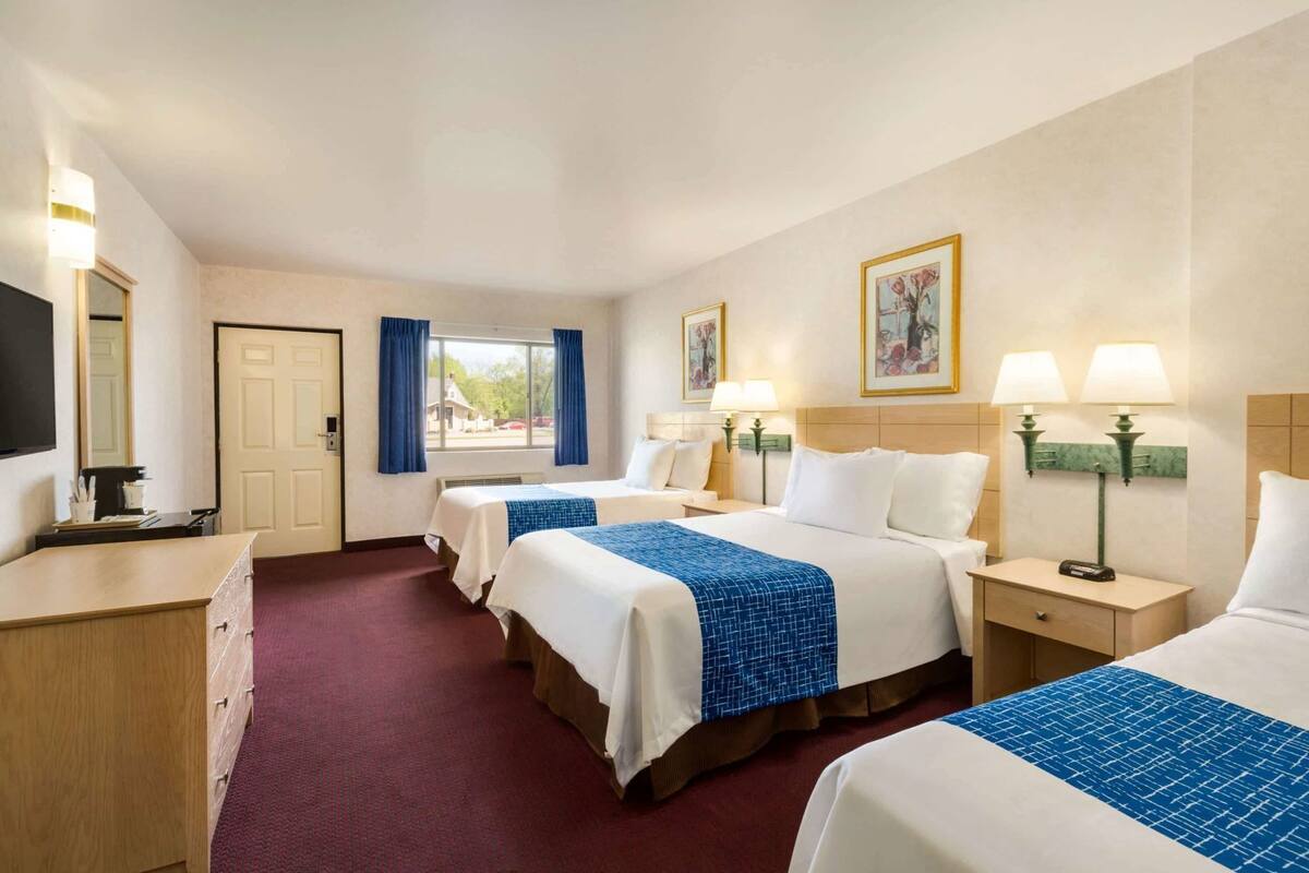 A hotel room with two beds, a desk, a chair, a TV, and a window with curtains.