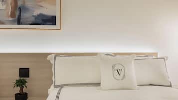 Una cama bien hecha con ropa blanca y detalles negros, una pequeña planta en maceta sobre la mesita de noche y un cuadro abstracto enmarcado en la pared.