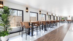 Un'area pranzo moderna con tavoli e sedie lunghe, ampie finestre e piante in vaso.