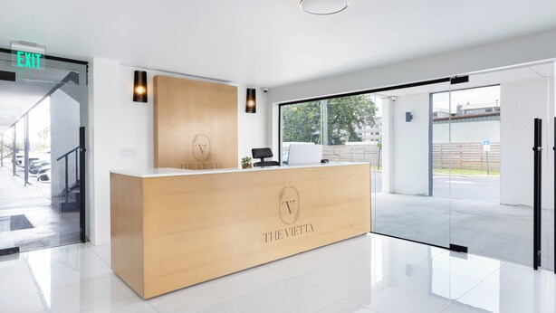 Una moderna reception con un logo, un computer e una porta vetrata che dà sull'esterno.