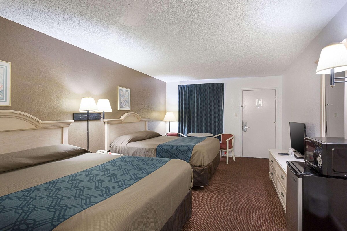 A hotel room with two beds, a desk with a computer, a TV, and a microwave.
