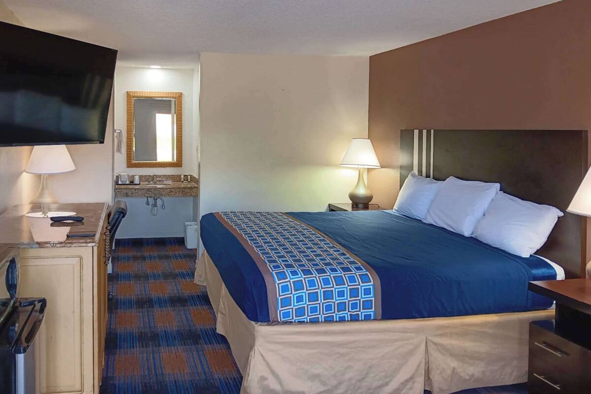 Une chambre d’hôtel avec un lit, un bureau, une télévision, un miroir et une salle de bain.
