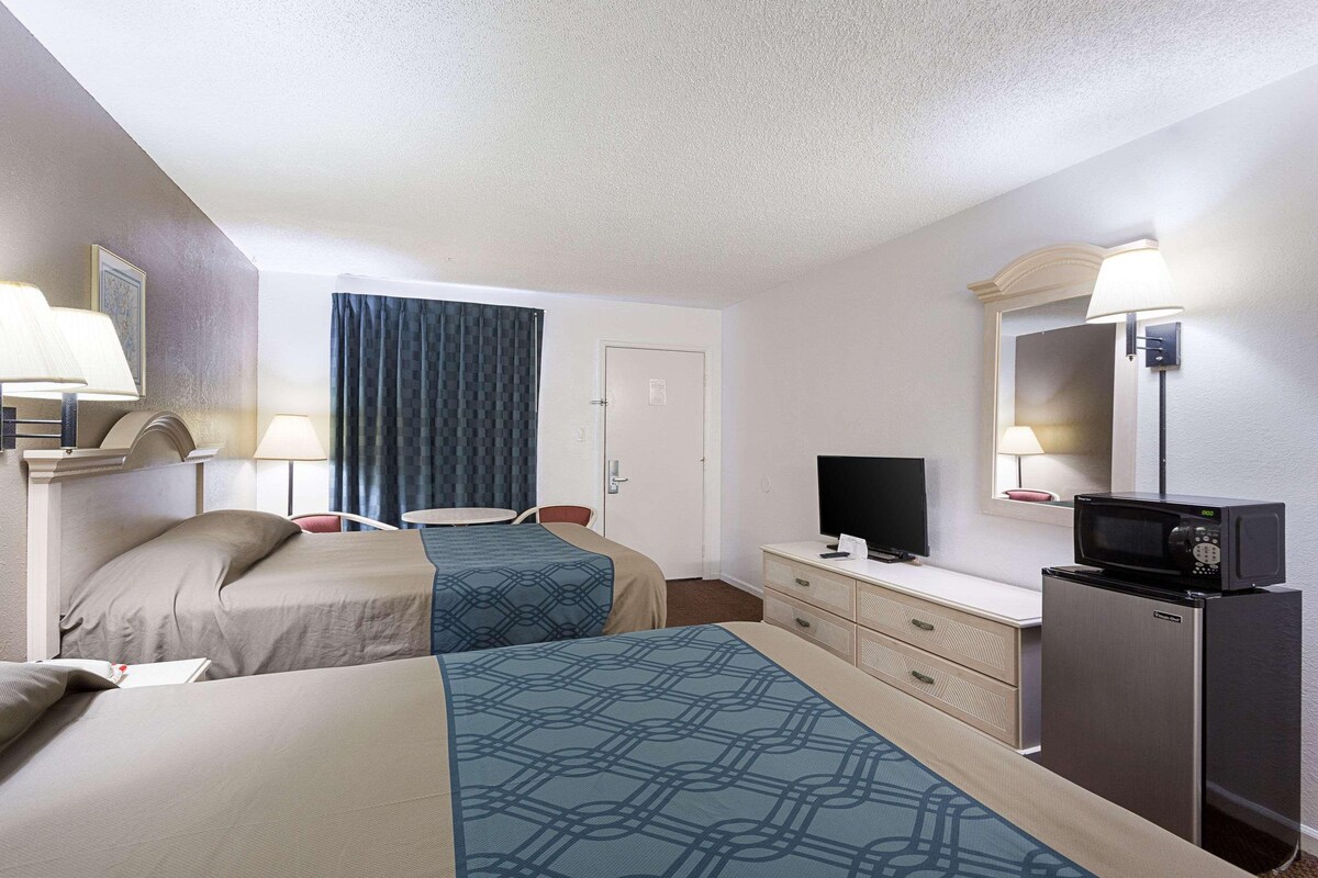 A hotel room with two beds, a desk with a television, a refrigerator, and a mirror.