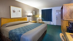 Hotelkamer met een groot bed, een bureau met een computer, een stoel, een bureaulamp, een telefoon, een fotolijstje en een raam met gordijnen.