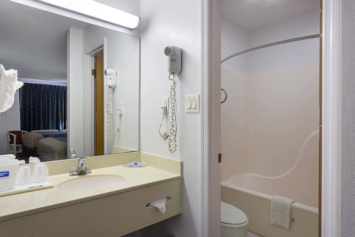 Une salle de bain d’hôtel équipée d’un lavabo, d’un miroir, d’un sèche-cheveux et d’une baignoire.