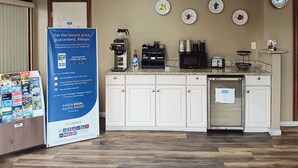 Een hotelkeuken met een koffieapparaat, magnetron en koelkast. Er is een bord met een reclame voor een spaarprogramma en een selectie reisbrochures.