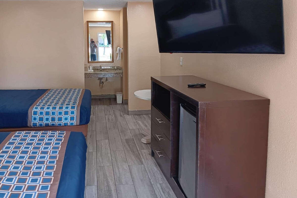 A hotel room with two beds, a TV, a small kitchenette, and a bathroom.