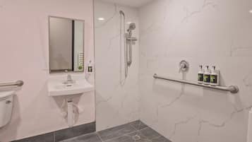 A bathroom with a sink, mirror, shower, and handrails.