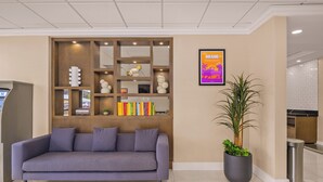 Un vestíbulo moderno con un sofá gris, un mueble de almacenamiento de madera con objetos decorativos, una planta en maceta y un cartel enmarcado que dice 'MIAMI'.