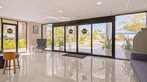 Zona de recepción de hotel con diseño moderno, que incluye puerta de cristal, mostrador de recepción y áreas de estar.