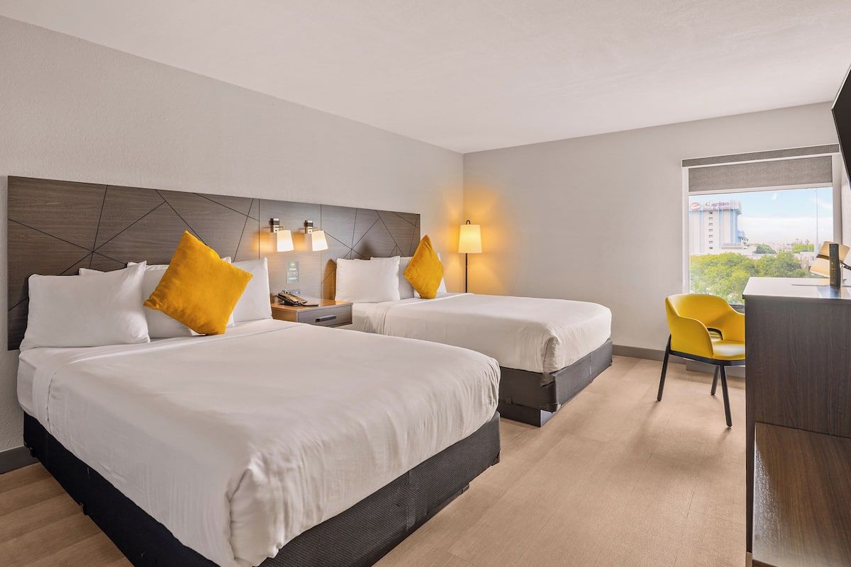 A hotel room with two beds, a desk, and a chair.