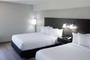 Two beds with crisp linens, a dark headboard, and a bedside table with a telephone and lamp.