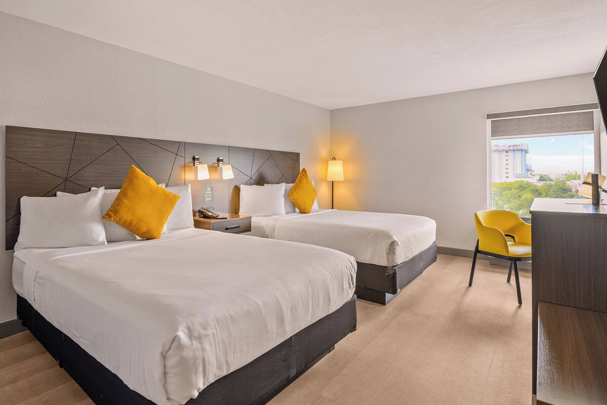 A hotel room with two beds, a desk, and a chair.