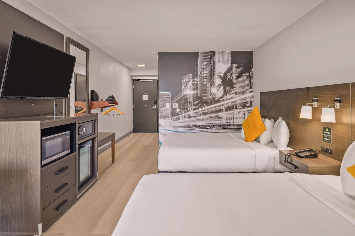 A hotel room with a bed, a TV, a desk with a microwave, and a cityscape wall mural.