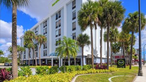Un hotel B&B con fachada blanca moderna, palmeras y un jardín bien cuidado.