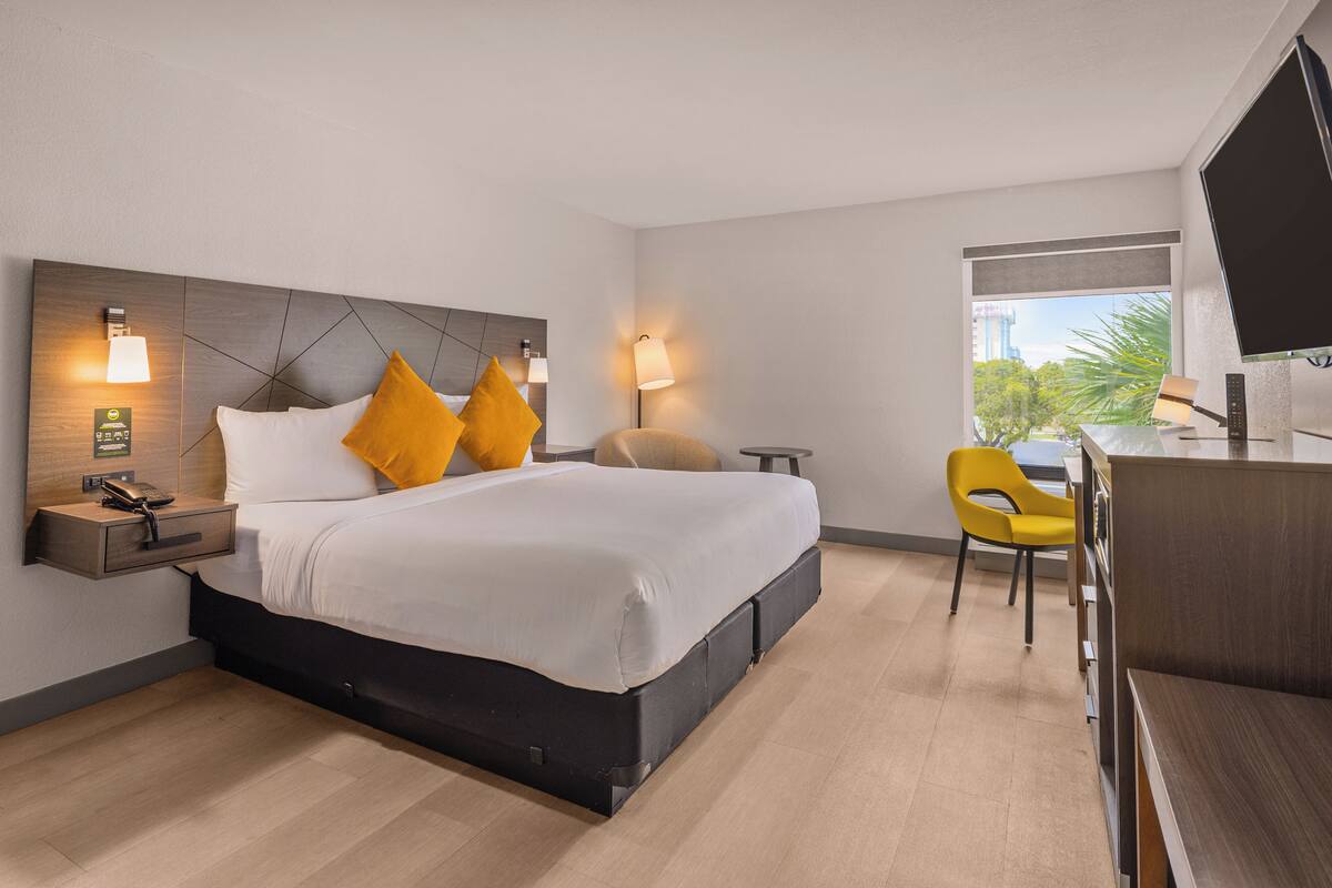 A modern hotel room with a large bed, bedside tables, a desk, and a TV.