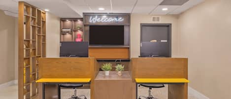 A modern office space with two desks, a large flat-screen TV, and a 'Welcome' sign above.