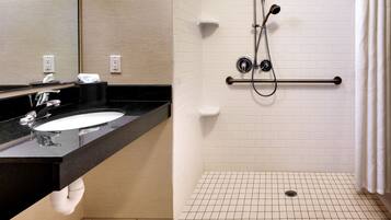 A modern bathroom with a black countertop sink, a mirror, a handheld showerhead, and a grab bar.