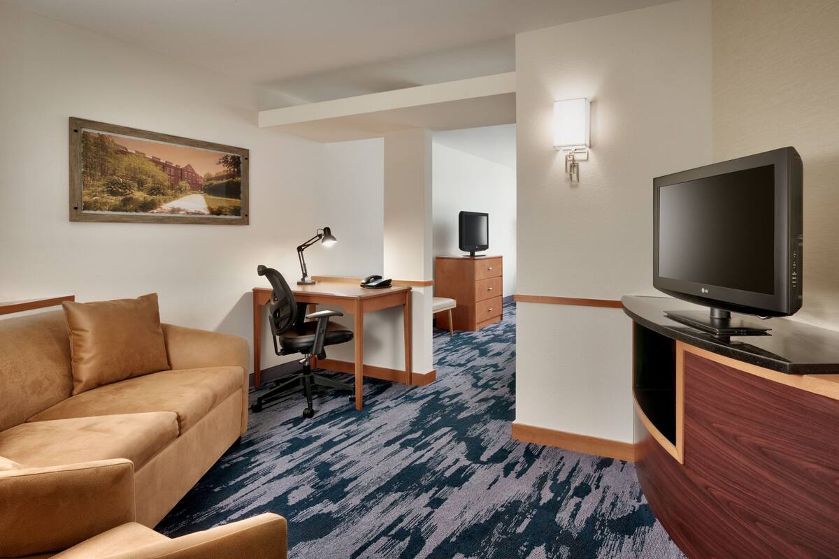 A hotel room with a sofa, desk, TV, and a painting on the wall.