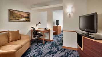 A hotel room with a sofa, desk, TV, and a painting on the wall.