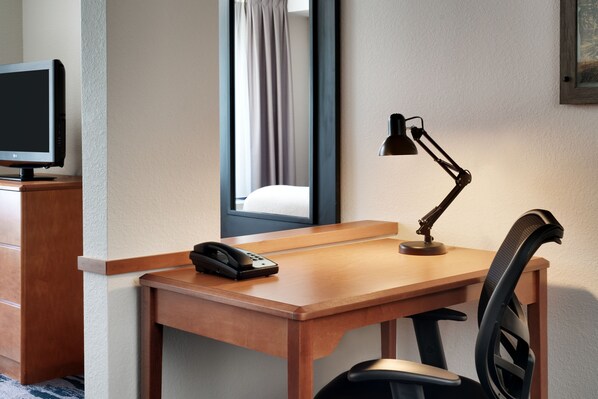 A hotel room with a wooden desk, a desk lamp, a telephone, and a chair. - Fairfield by Marriott Inn & Suites Tallahassee Central (Tallahassee)