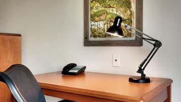 A wooden desk with a black desk lamp, a telephone, and a framed picture of a forest on the wall.
