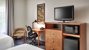 A hotel room with a bed, a desk with a chair, a television, a microwave, and a refrigerator.