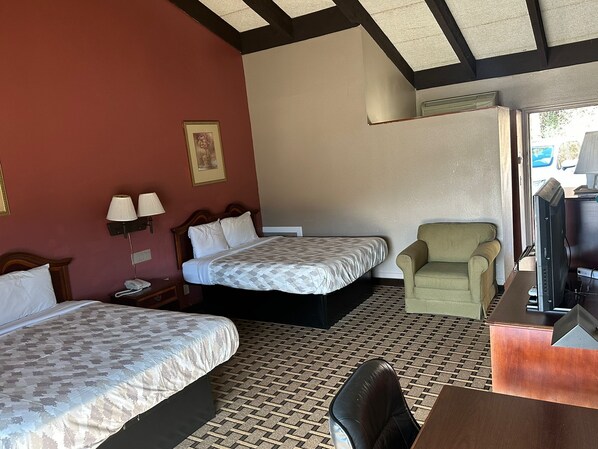 A hotel room with two beds, a chair, a desk, and a television.