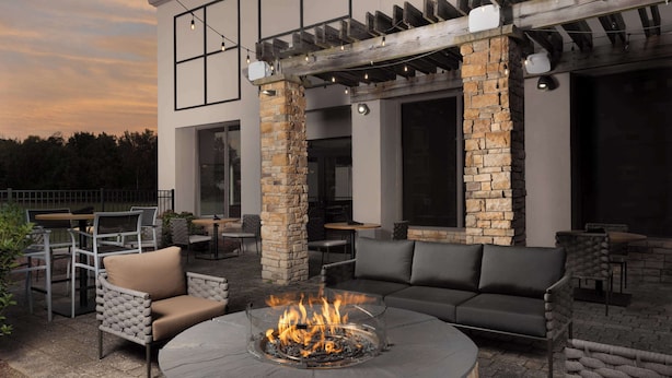 An outdoor patio with a round fire pit, seating area, and stone pillars.