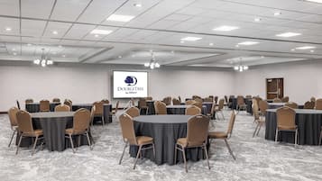 A conference room with round tables and chairs, a projector screen, and a ceiling with recessed lighting.