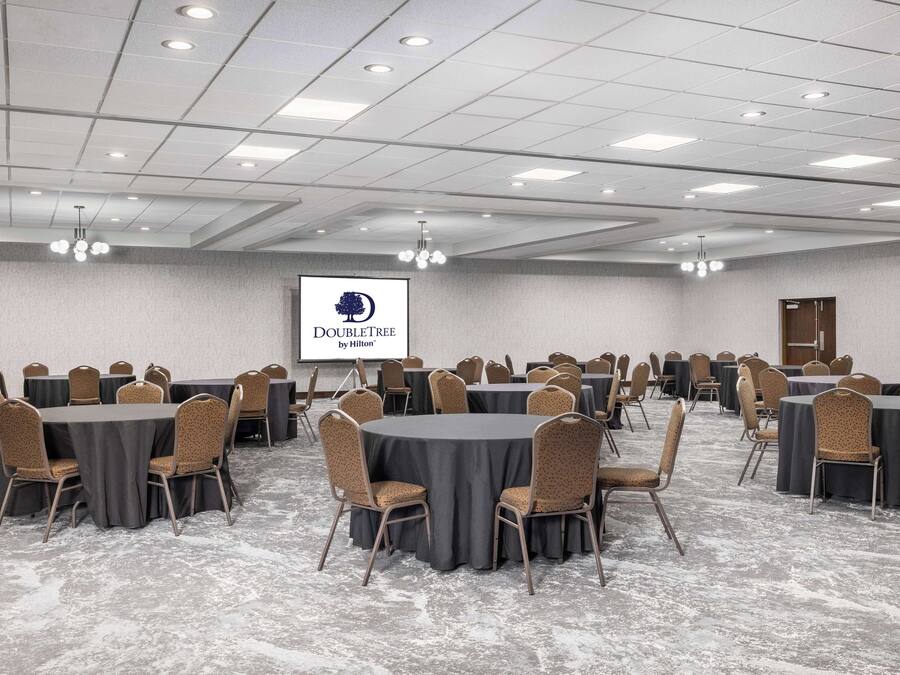 A conference room with round tables and chairs, a projector screen, and a ceiling with recessed lighting.