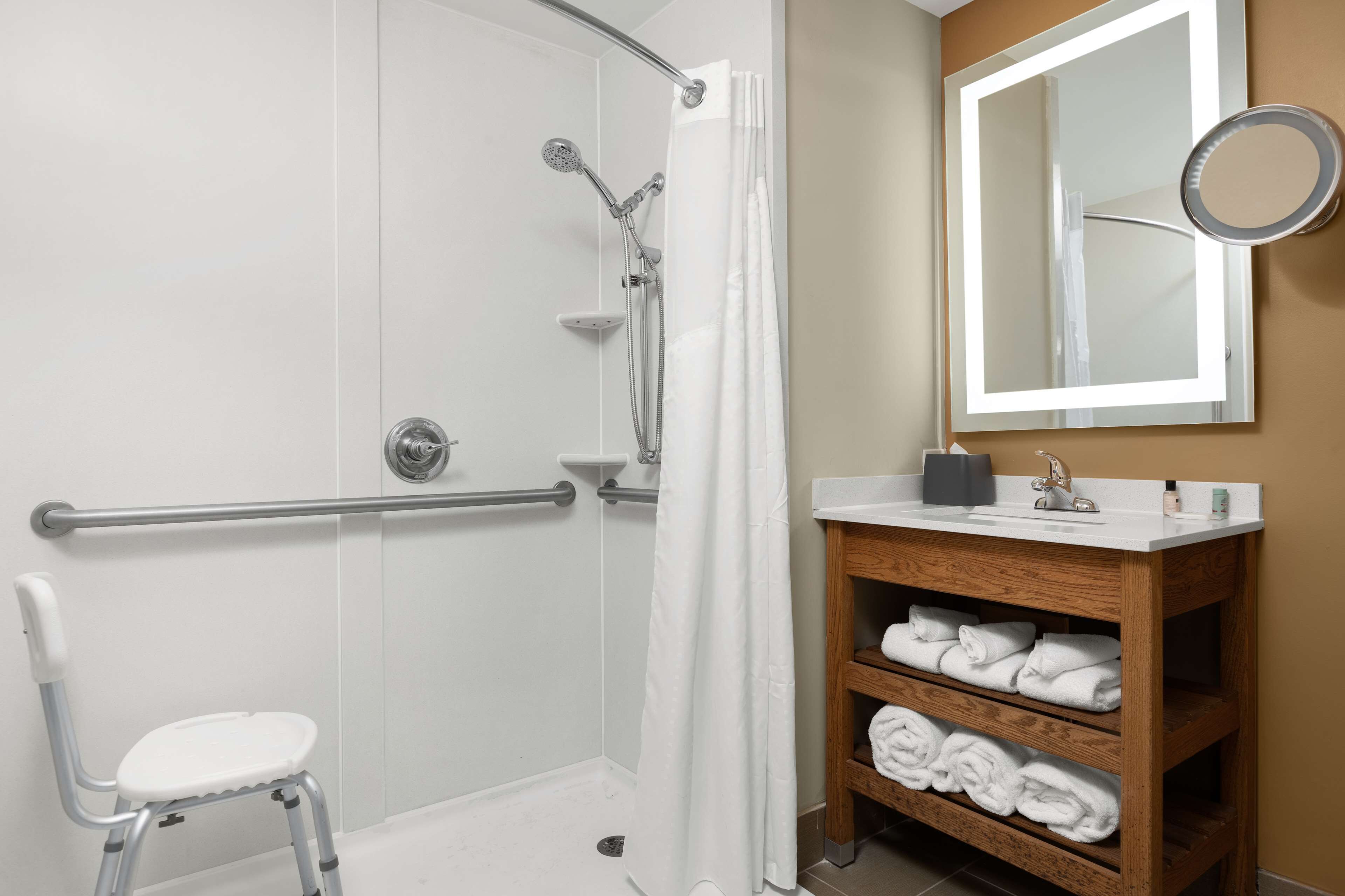 A bathroom with a glass shower enclosure, a white toilet, a vanity with a mirror, and a shelf with towels.
