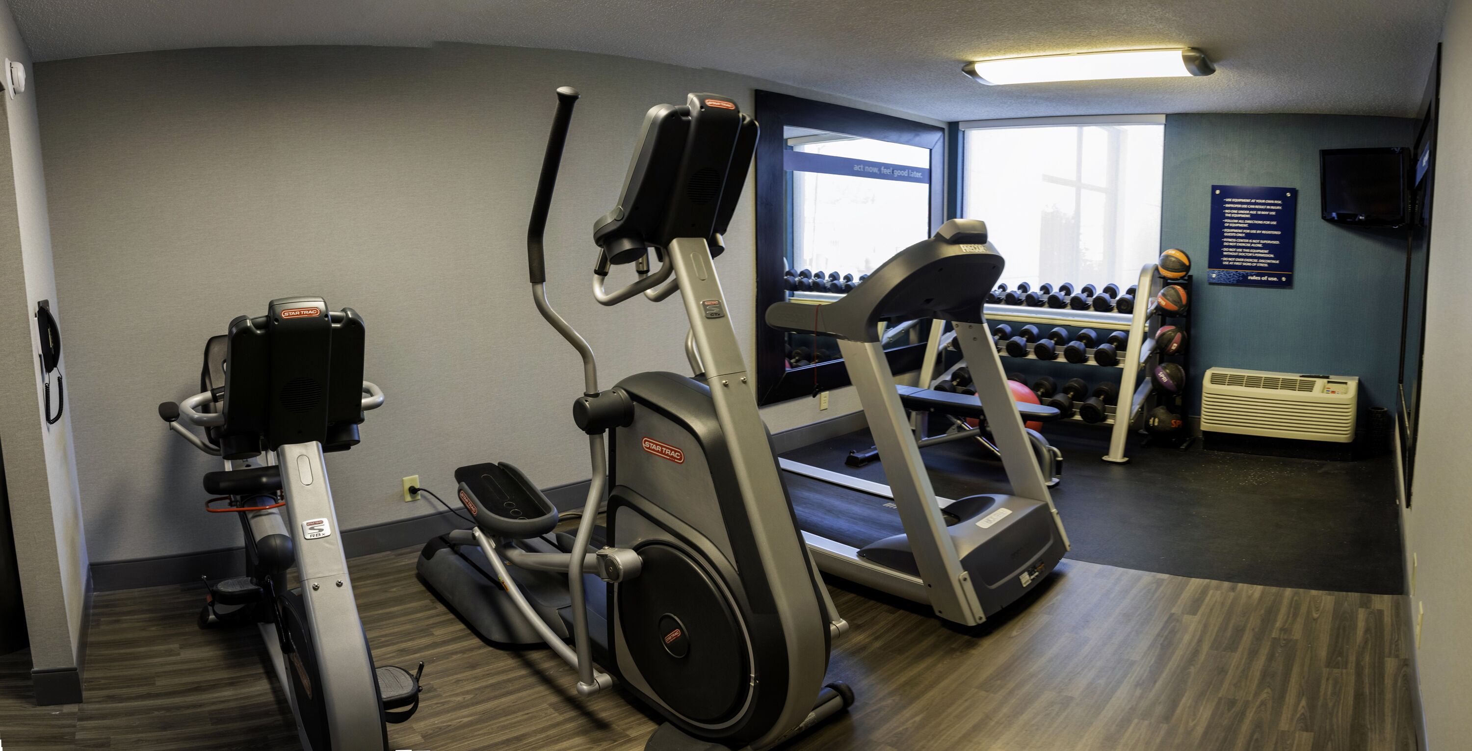 A gym with an elliptical, a treadmill, and a wall of dumbbells.