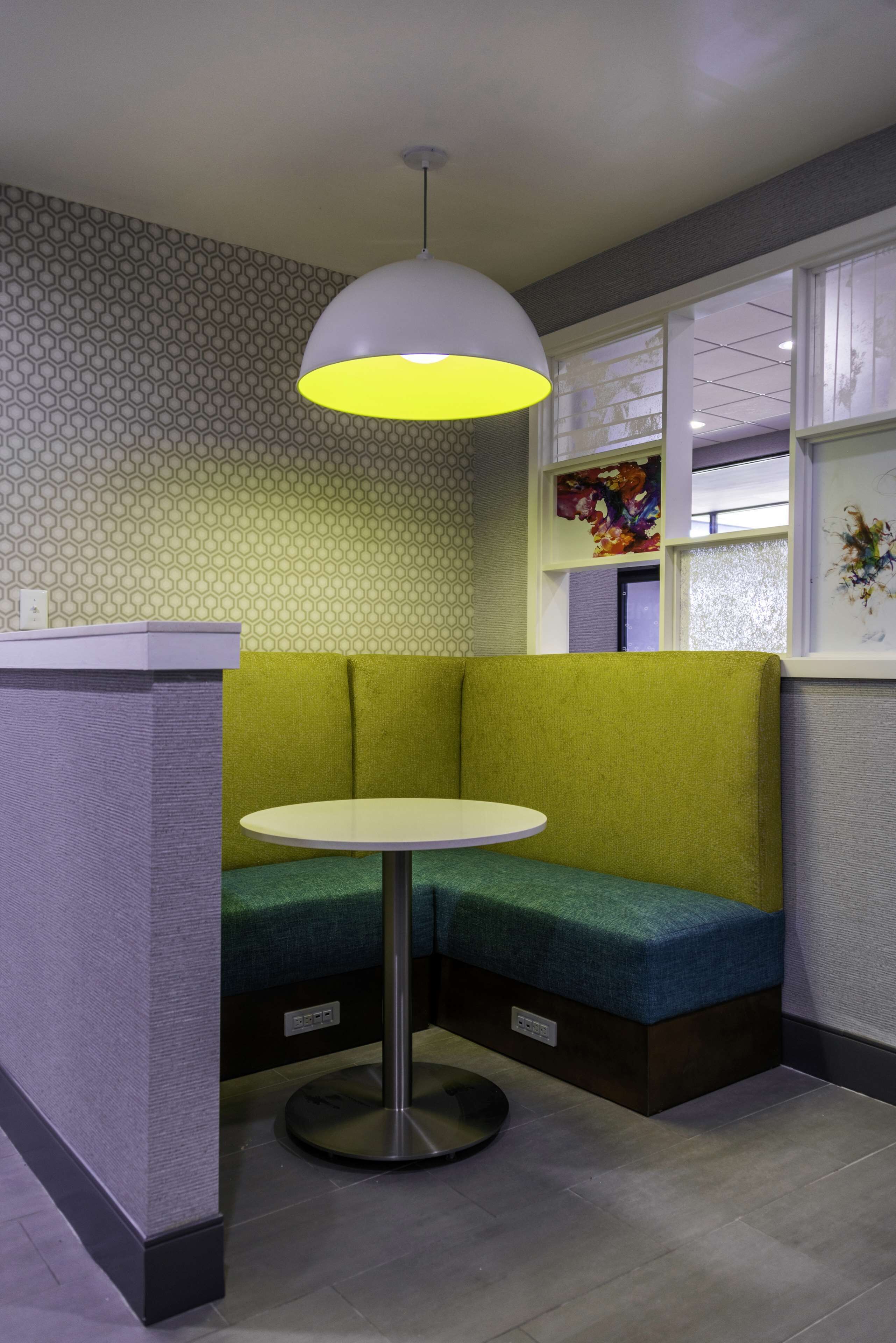 A corner seating area with a round table, a green cushioned bench, and a pendant light.