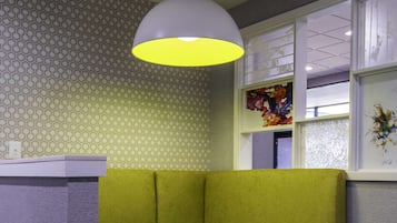 A corner seating area with a round table, a green cushioned bench, and a pendant light.