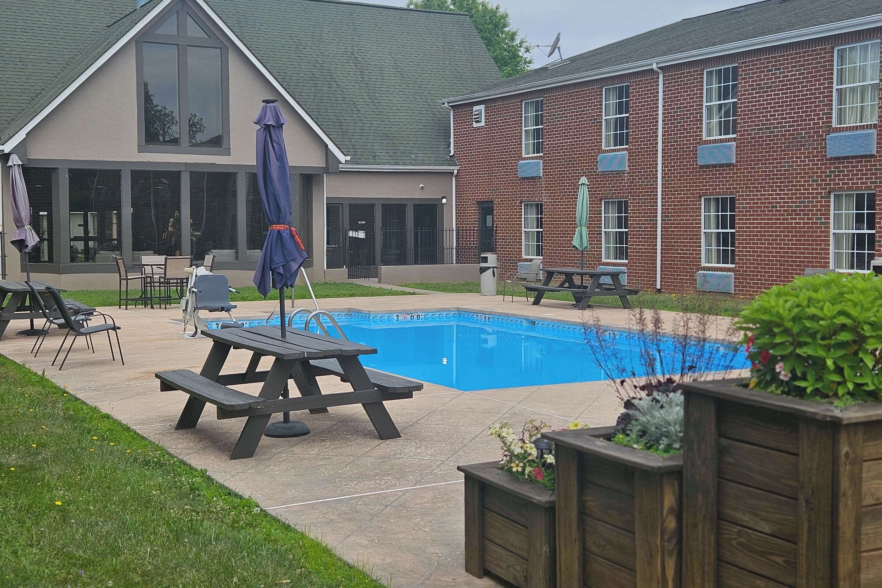 A backyard with a swimming pool, picnic tables, and lounge chairs.
