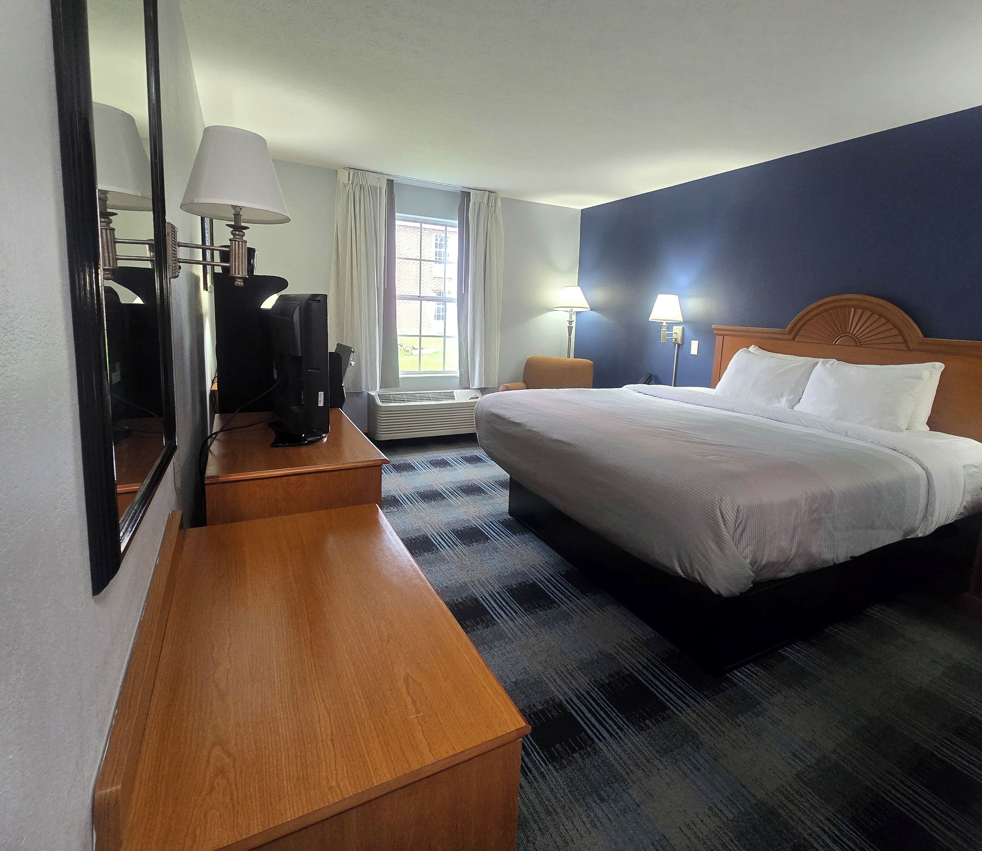 A hotel room with a bed, bedside lamps, a desk, and a large mirror.