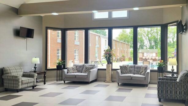 A spacious room with large windows, a grey sofa set, a patterned armchair, and a small table with a lamp.