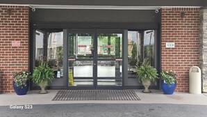 A building entrance with a brick facade, a black awning, and potted plants.