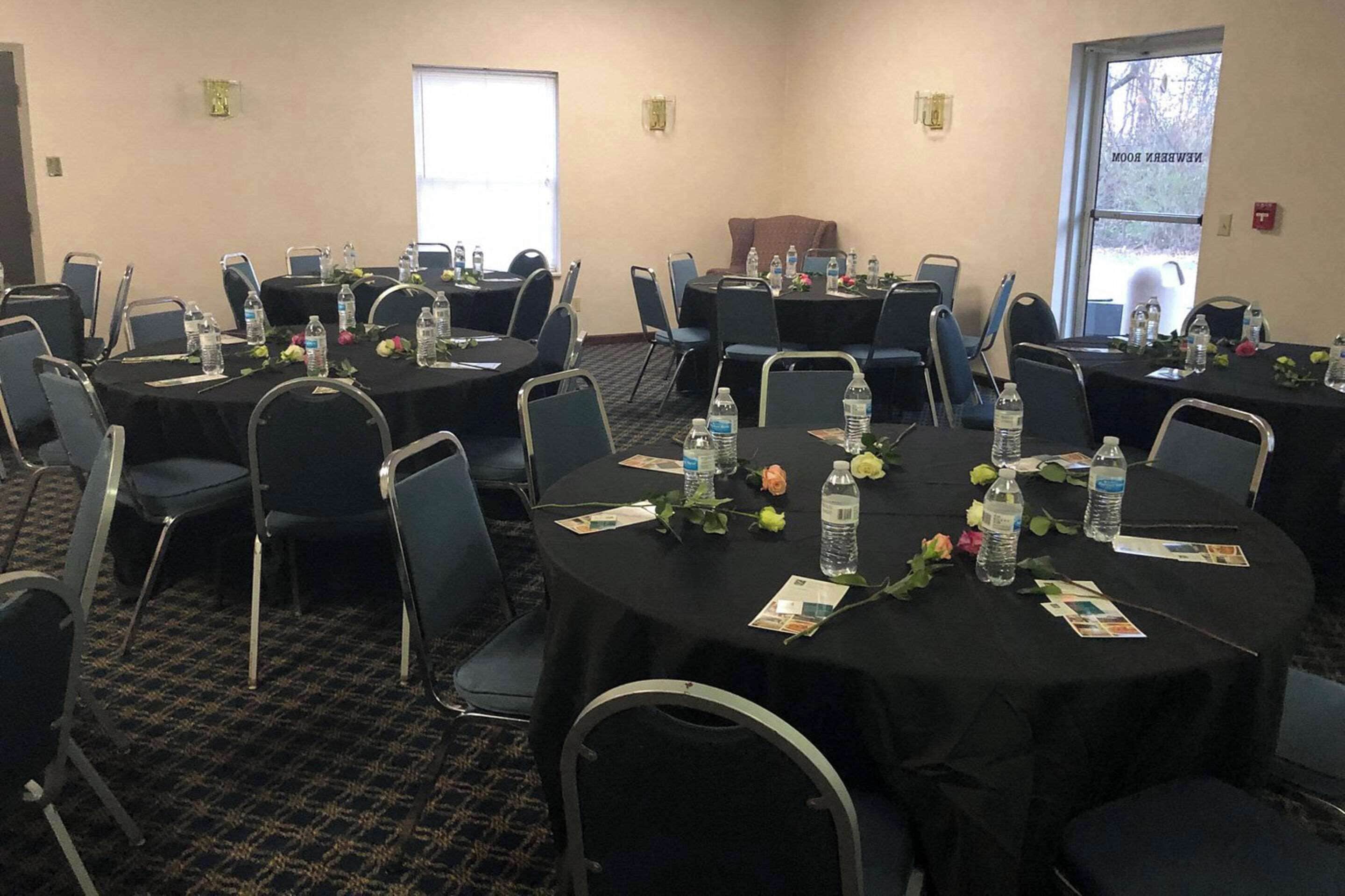 A conference room with multiple tables, chairs, water bottles, and flower arrangements.