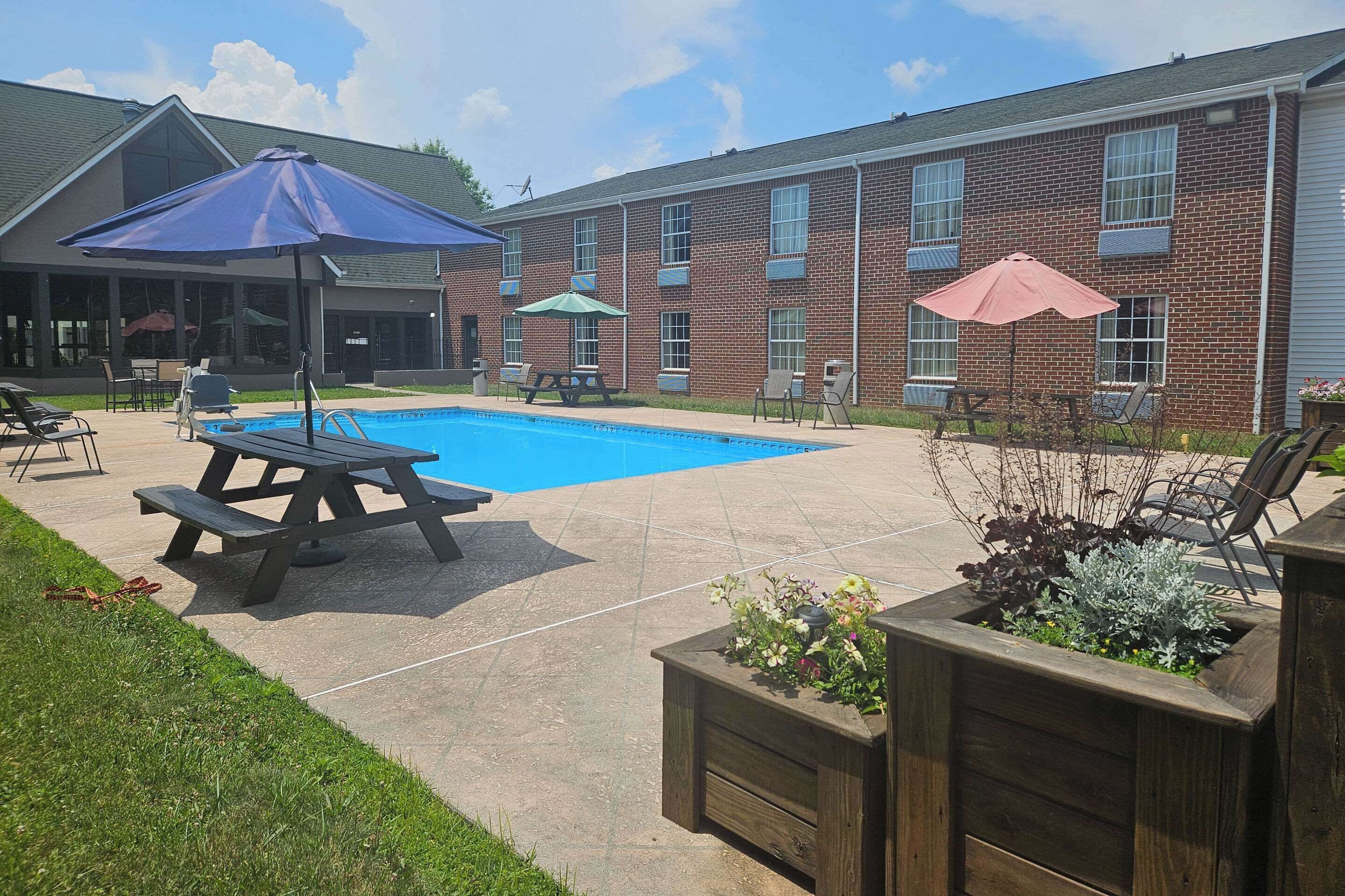 Un patio trasero con piscina, mesas de picnic y mobiliario de exterior.